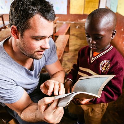 Blanke man kijkt samen met een Ugandese jongen in een schrift.