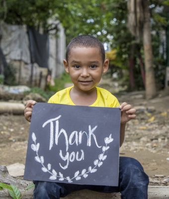 Een jongen in een geel shirt houdt een bord vast met de tekst Thank you.