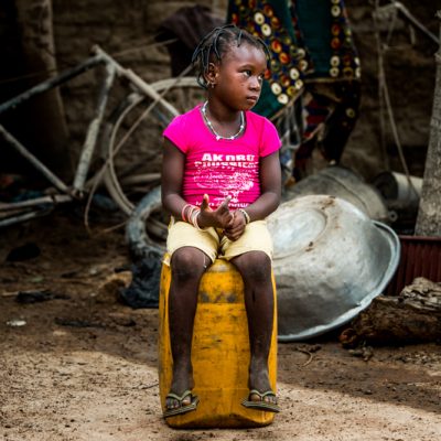 Meisje in roze shirtje en korte broek zit op geel vat staart naast zich met op de achtergrond troep