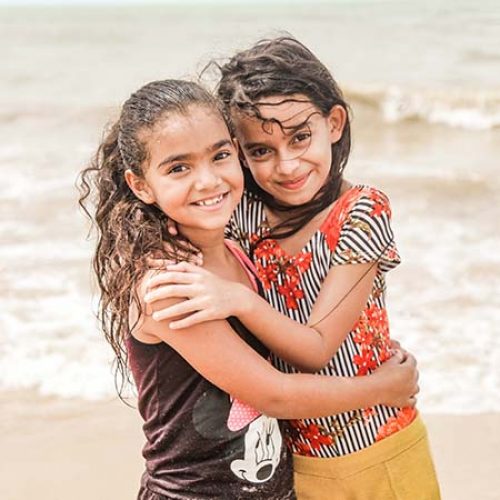 Twee meisjes staan op het strand en omhelzen elkaar.
