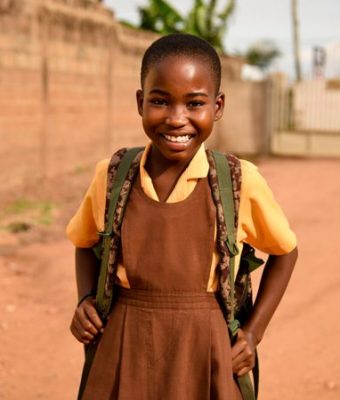 Vrolijk meisje uit Kenia in schooluniform met rugtas op haar rug