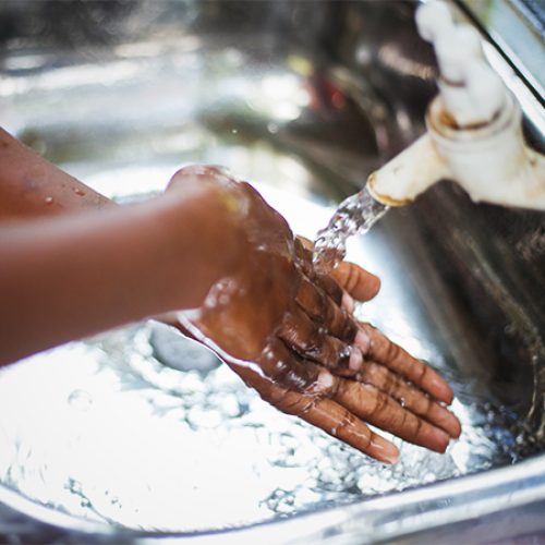 Een kind wast zijn handen bij een kraan.